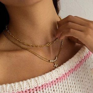 Détail macro du collier double rang en acier doré avec pendentif croix en perles sur cou