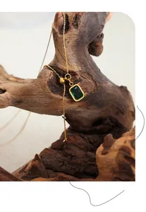 Detail of gold necklace with emerald green pendant and BABY tag on rustic wood background