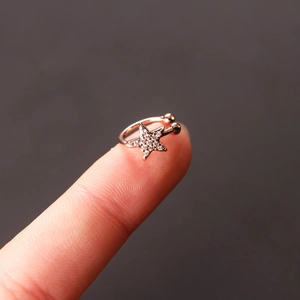 Macro shot of tiny rose gold star ear cuff with white zircon micro-inlay on fingertip