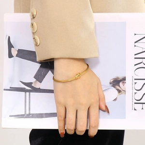 Bracelet jonc minimaliste doré en acier inoxydable avec nœud élégant porté par un mannequin