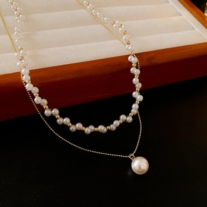 Vue macro d'un collier de perles à double rangée avec chaîne dorée sur présentoir blanc