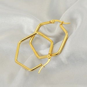 Polished gold stainless steel hexagonal hoop earrings on luxury white silk fabric
