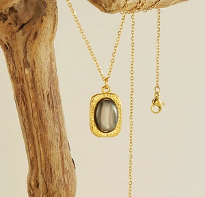 Close-up of vintage 18K gold square pendant with grey natural stone on a branch