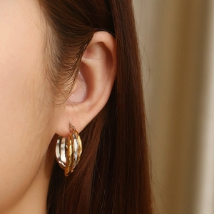 Close-up of tricolor intertwined hoop earrings in gold silver and rose gold on model