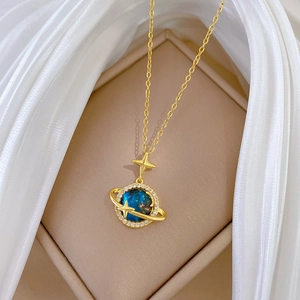 Dettaglio macro di una collana dorata con ciondolo a forma di pianeta blu e stelle brillanti