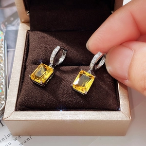 Macro detail of silver dangle earrings with rectangular yellow gemstones in a velvet box
