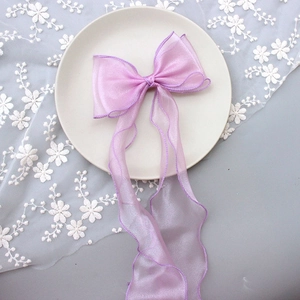 Close-up of a large pink organza ribbon bow hairclip on white lace and floral decor