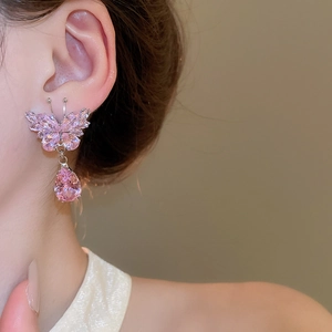 Detail of pink crystal butterfly earring with teardrop pendant worn on model's ear