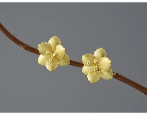 Macro shot of gold crabapple flower stud earrings with brushed metal texture on a branch