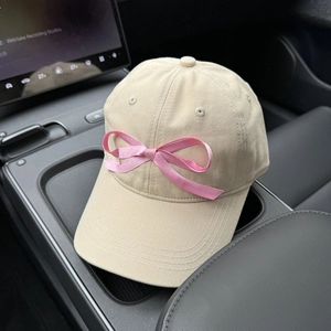 Detail of a beige cotton baseball cap with a pink satin bow in a car interior setting