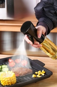 Kitchen oil sprayer bottle misting olive oil onto a steak in a frying pan