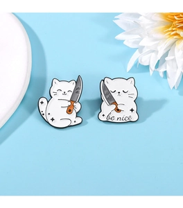 Detail of a cute white cat enamel pin holding a knife with 'be nice' text on blue background