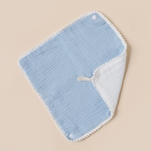 Detail view of double-sided cotton baby bib with pompom trim, snap button and lanyard