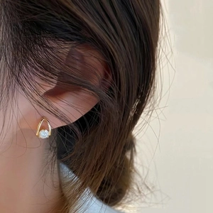 Close-up of a gold teardrop earring with round moissanite stone worn by a model