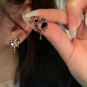 Close-up of heart-shaped silver earrings with black gemstones and liquid metal texture