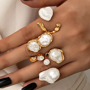 Detailed view of irregular gold rings with white baroque pearls on a hand