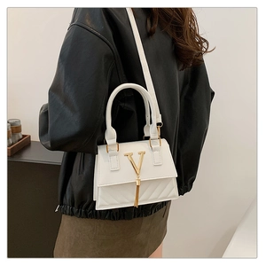 Close-up of white square handbag with golden V-clasp and tassel on a leather jacket