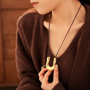 Détail d'un collier pendentif doré en forme de U avec un cordon noir ajustable minimaliste