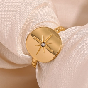 Detailed view of 18K gold plated starburst ring with crystal on silk fabric background