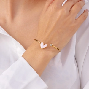 Detail of a gold open bangle with a pink marble heart and a sparkling cubic zirconia stone
