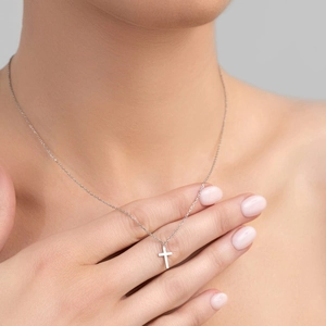 Close-up of minimalist silver cross pendant necklace worn by a model in soft light