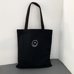 Close-up of minimalist black canvas tote bag with white line smiley face and sturdy handles