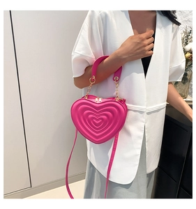 Detail der rosa Herz-Tasche mit geprägten Kreisen und goldener Kette am Modell