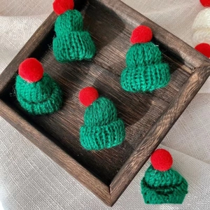 Close-up of green mini knitted Christmas hats with red pom poms on a rustic background