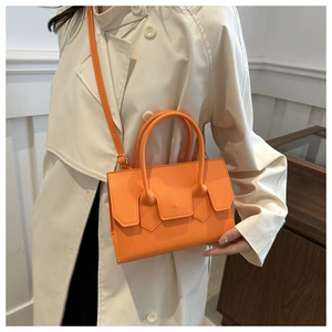 Detail of orange PU leather handbag with long strap on a beige trench coat model