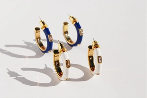 Detail of C-shaped enamel hoop earrings with blue and white accents and zircon inlays