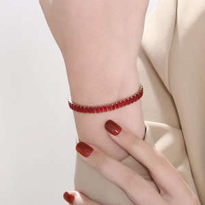 Luxury gold tennis bracelet with emerald-cut red zircons worn on a female wrist