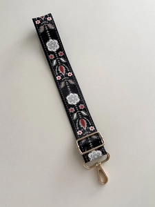 Detail of 38mm black embroidered nylon bag strap with colorful floral patterns and gold hardware
