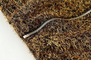 Macro detail of bronze metallic tinsel fabric and silver metal zipper on pilot jacket