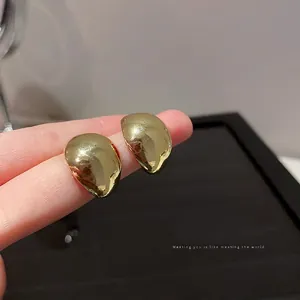 Minimalist golden bean stud earrings with polished mirror finish held on finger
