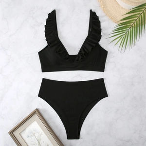 Close-up of black ribbed bikini with ruffled straps and high waist on marble background