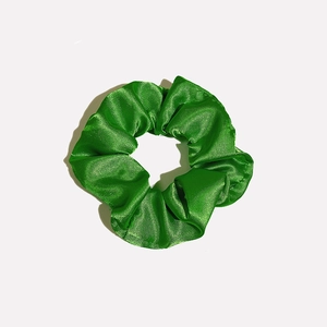 Detailed view of emerald green satin scrunchie with soft pleated texture and silky finish