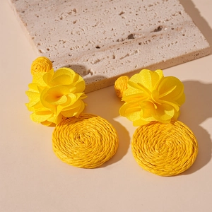 Detailed close-up of yellow woven raffia flower earrings with bohemian vacation style