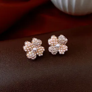 14K gold plated four-leaf clover flower earrings with pearls and crystals on leather background