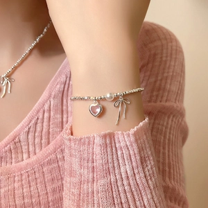 Detailaufnahme von Perlenarmband mit rosa Herzstein und silbernem Schleifenanhänger