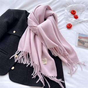 Detail of pink cashmere-like scarf with fringe and 2023 brand label on black coat
