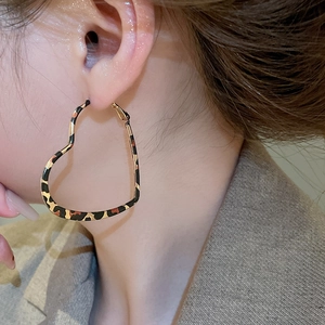 Side view of model wearing large leopard print heart-shaped hoop earrings in gold