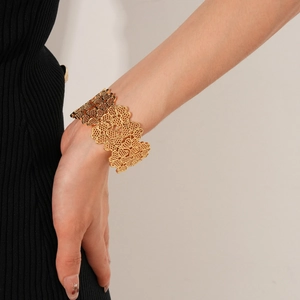 Detailed view of an ornate gold-tone open cuff bracelet with hollow floral clover patterns