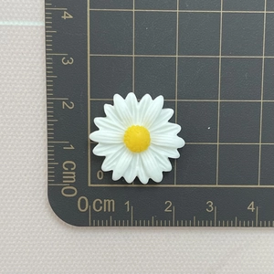 Detailed size measurement of 2.3cm white resin daisy charm on a black grid cutting mat