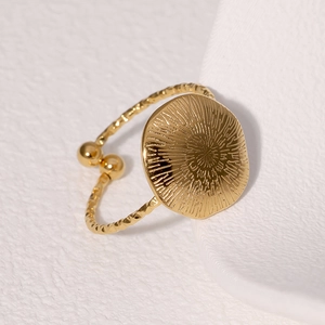 Detail of gold-plated open ring featuring a radial texture face and twisted band design