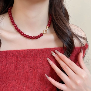 Close-up of red beaded necklace with a gold diamond-set ring pendant on a red sweater