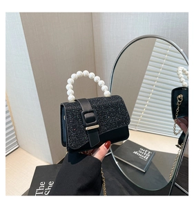 Close-up of black glitter mini flap bag with white pearl handle and gold chain strap