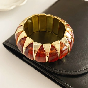 Close-up of amber resin and gold metal geometric elastic bracelet on black leather texture