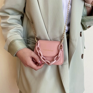 Mini pink jelly crossbody bag with chunky acrylic chain and gold strap on a sage green suit