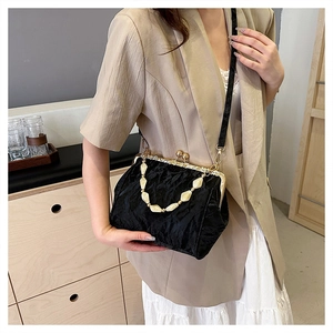 Model wearing a black textured shell bag with beaded chain and gold metal frame