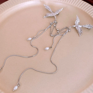 Detail of silver phoenix brooch with faux pearls and long tassels on a ceramic plate